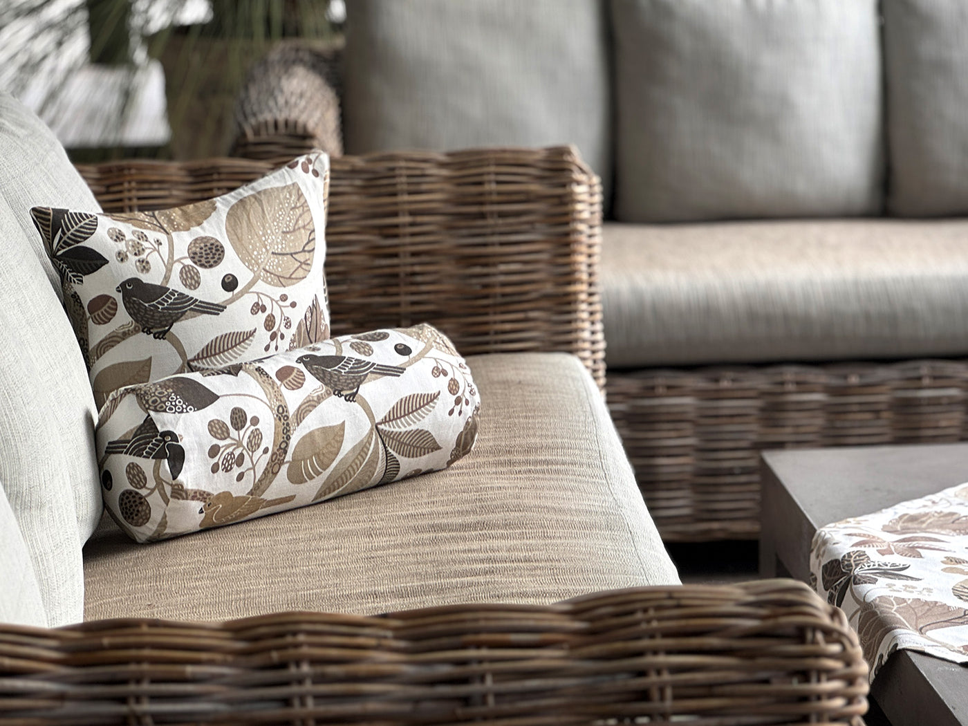 Dekorative Kissen mit Vogel- und Blättermuster in Naturtönen auf einem Sofa.
