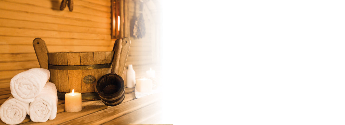 Eine Holzsauna mit einem Holzeimer, einer Schöpfkelle, aufgerollten weißen Handtüchern, die auf einer Bank angeordnet sind und eine gemütliche, entspannende Atmosphäre schaffen. Die linke Seite des Bildes verschwindet in Weiß.
