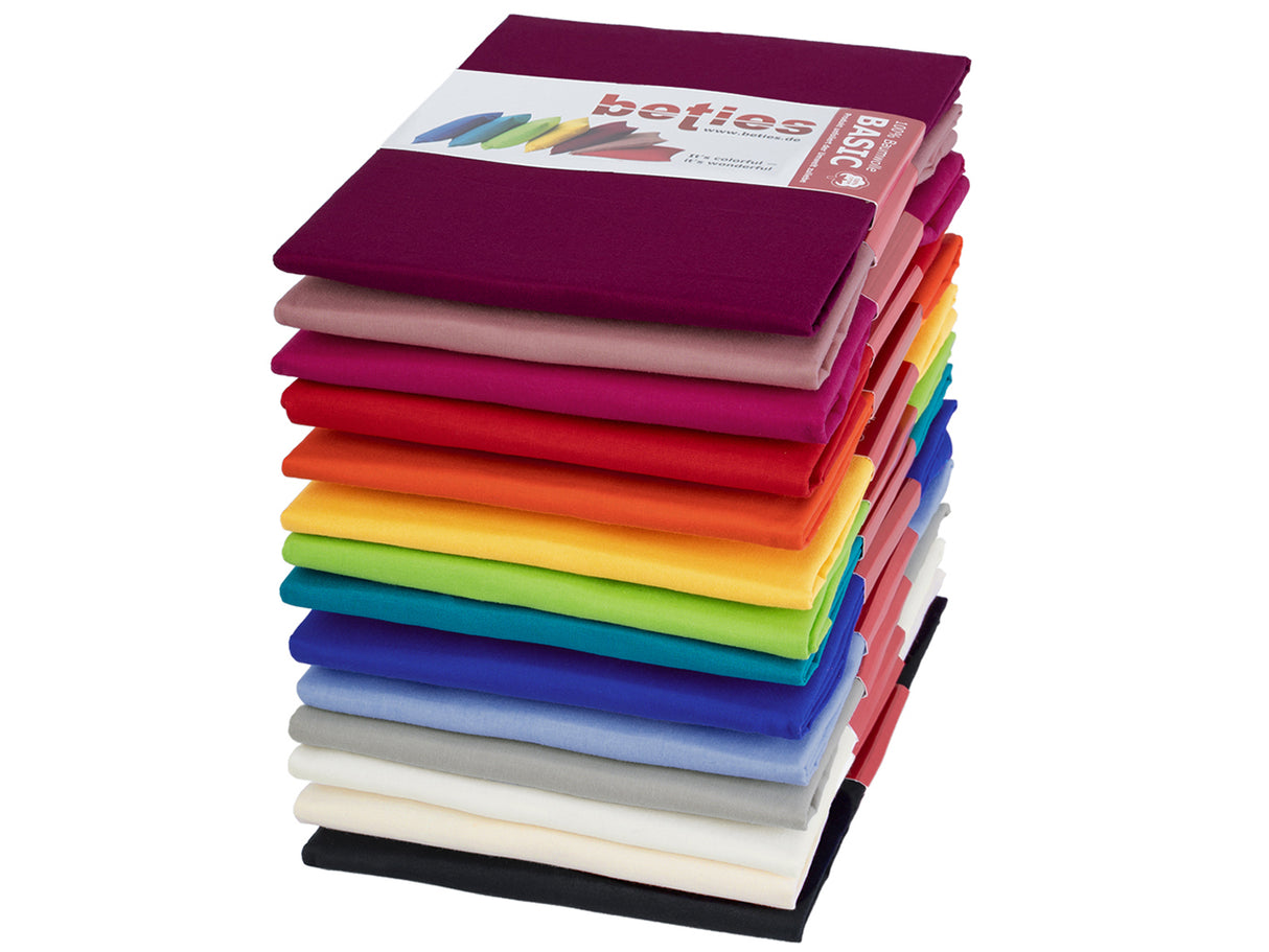 Ein Stapel gefalteter Kissenhuellen in kraeftigen Uni-Farben Schwarz, Hellbeige, Weiss, Hellgrau, Hellblau, Royal-Blau, Petrol, Apfelgruen, Gelb, Orange, Rot, Pink, Altrosa und Weinrot.