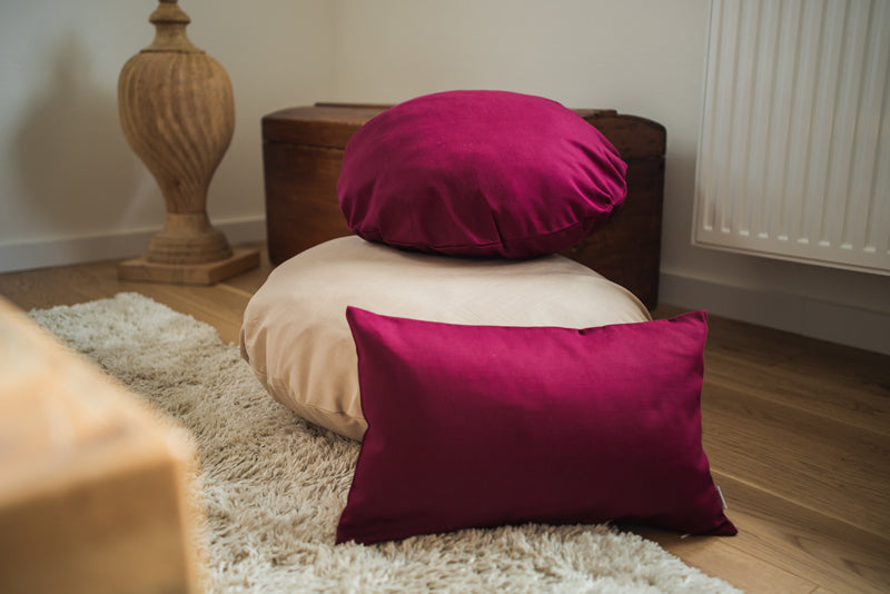 Zwei runde und ein rechteckiges Kissen in den Farben Beige und Hibiskus-Beere in einem Wohzimmer dekoriert.