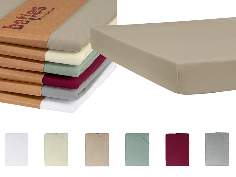 Ausschnitt einer beigen Matratze auf einem weissen Hintergrund. Daneben ein Stapel mit gefalteten Kissenbezuegen in den Uni-Farben Wei�, Hellgrau, Weinrot, Gruen, Natur und Beige.