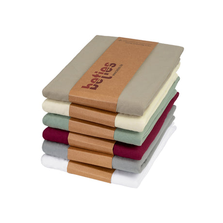 Ein Stapel gefalteter Bettlaken in verschiedenen Farben, darunter grün, beige, cremefarben, weinrot, grau und weiß, zusammengehalten von einer braunen Papphülle mit der Aufschrift betties, auf weißem Hintergrund.
