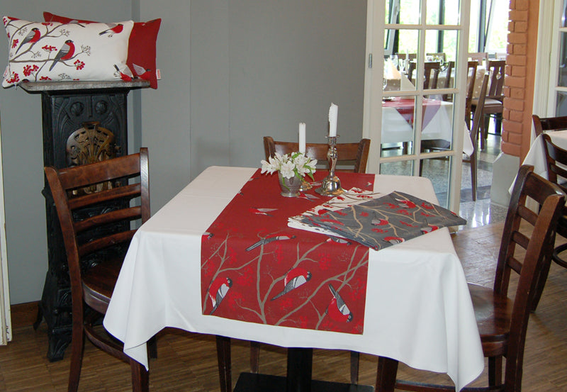 Roter Tischlaeufer mit rot-grau-schwarzen Voegeln auf einem Tisch. Teilweise fliegend und teilwiese sitzen die Voegel auf Zweigen mit roten Beeren.