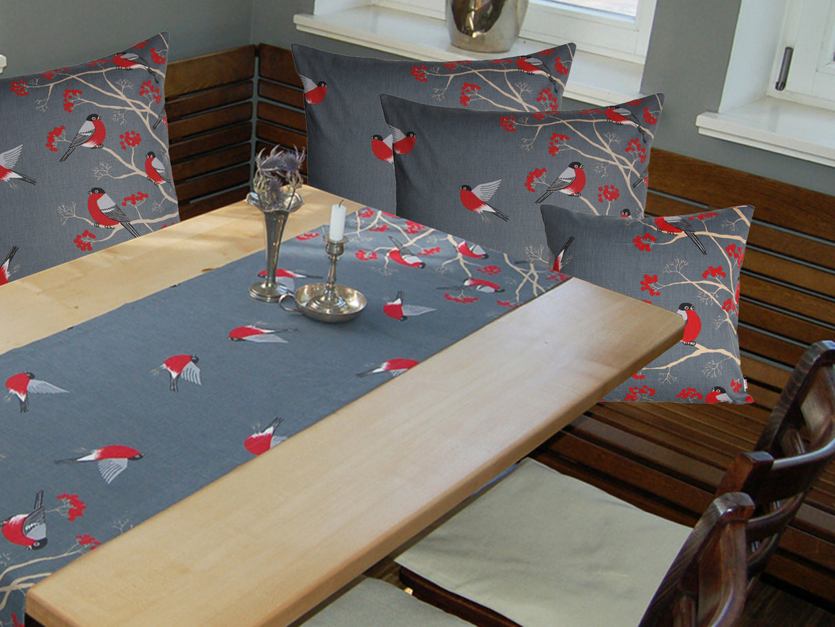 Grauer Tischlaeufer mit rot-grau-schwarzen Voegeln auf einem hellen Holztisch. Teilweise fliegend und teilwiese sitzen sie auf Zweigen mit roten Beeren.