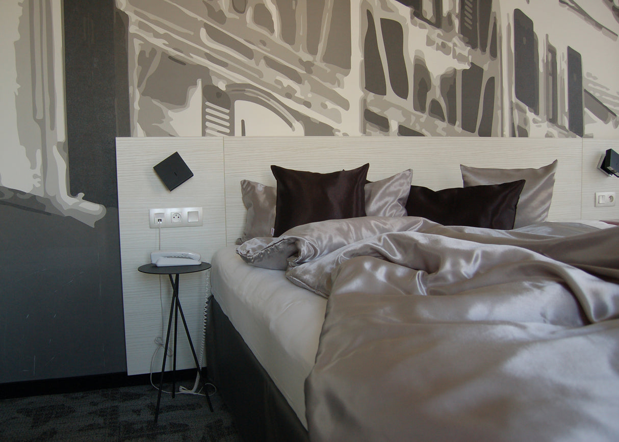 Schlafzimmer mit grau weißer moderner Tapete auf dem Bett lieg eine edle Glanz Satin Bettwäsche in grau