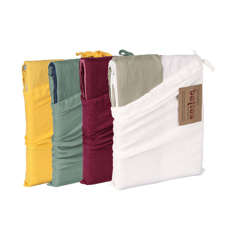 Vier gefaltete Leinen-Decken stehen aufrecht in einer Reihe. Die Decken sind gelb, grün, bordeauxrot und weiß. An der weißen Decke auf der rechten Seite ist ein braunes Papieretikett befestigt.