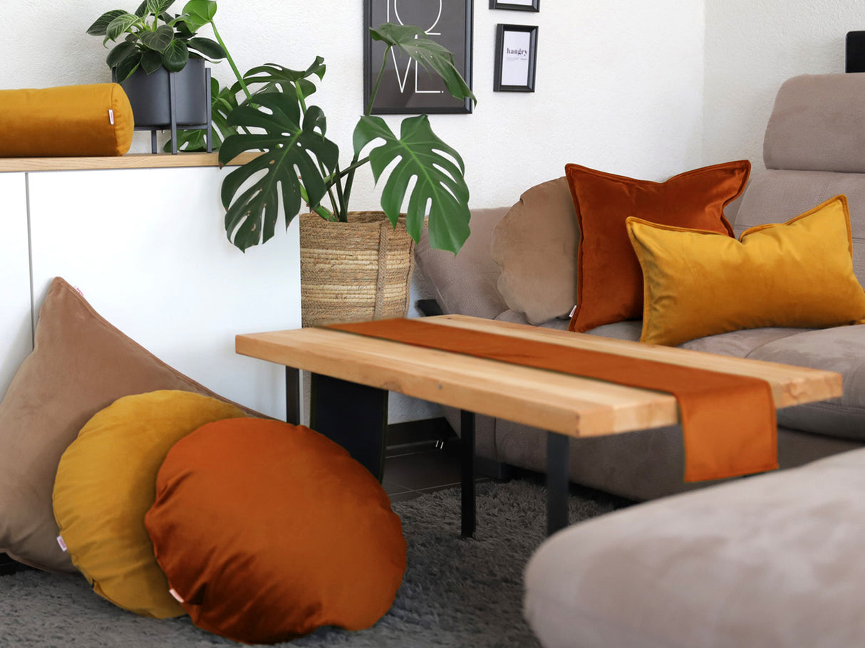 Curry-senf-gelbe, braun-beige und rost-orange Samt Kissenbezuege und ein rost-oranges Tischband sind in einem Wohnzimmer dekoriert.
