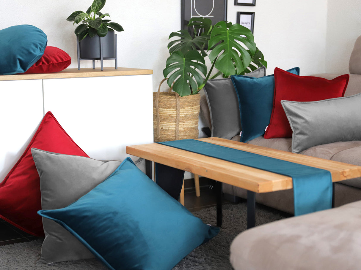 Karmin-rote, graue und petrol-farbene Samt Kissenbezuege und ein petrol-farbenes Samt Tischband sind in einem Wohnzimmer dekoriert.