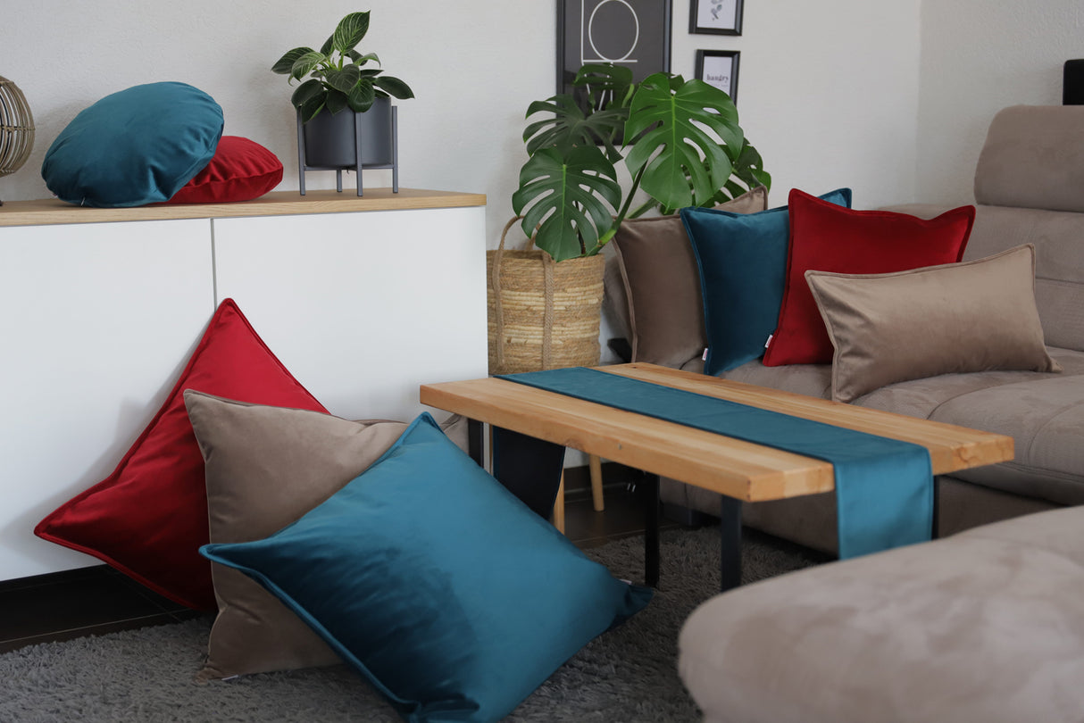 Karmin-rote, taupe-farbene und petrol-farbene Samt Kissenbezuege und ein petrol Samt Tischband sind in einem Wohnzimmer dekoriert.