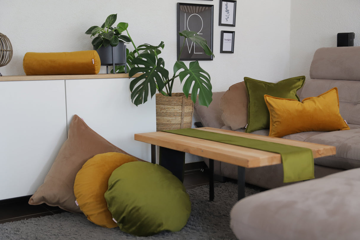 Curry-senf-gelbe, braun-beige und mai-gruene Samt Kissenbezuege und ein mai-gruenes Tischband sind in einem Wohnzimmer dekoriert.
