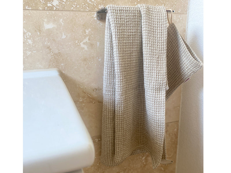 Vor einer Wand aus Marmor haengt ein Handtuch und ein Waschhandschuh, beide aus beigem Waffelpique.