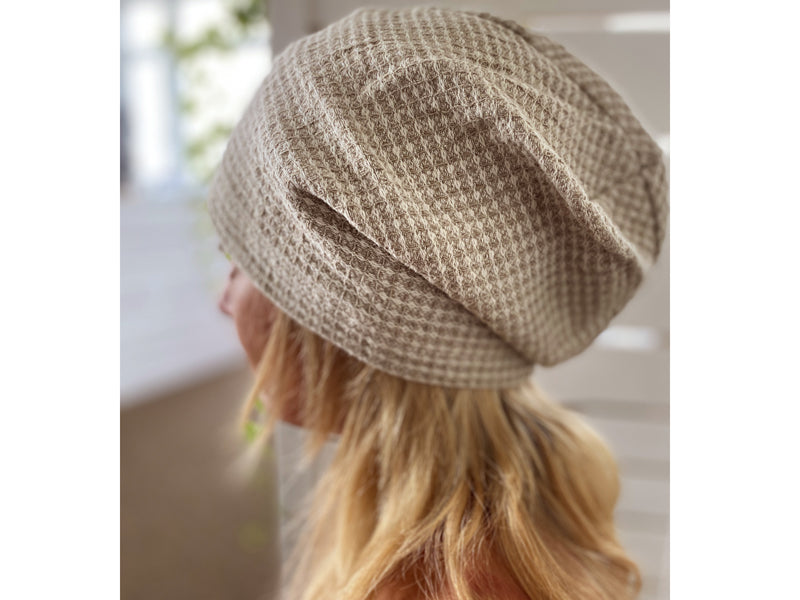 Eine blonde Frau hat eine Sauna-Muetze aus beigem Waffelpique-Stoff auf dem Kopf.