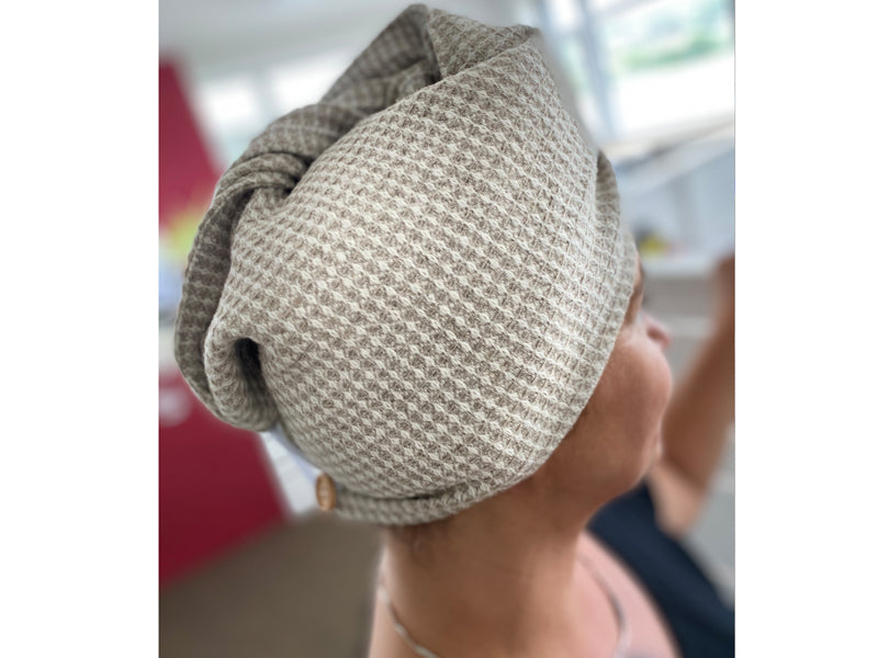 Eine Frau mit einem Haarturban aus beigem Waffelpique-Stoff auf dem Kopf.