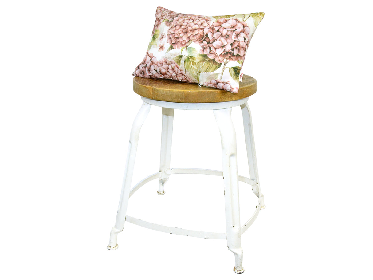 Auf einem Hocker liegt ein weisser Kissenbezug im Landhausstil, bedruckt mit rosa/pinken Hortensien-Blueten.