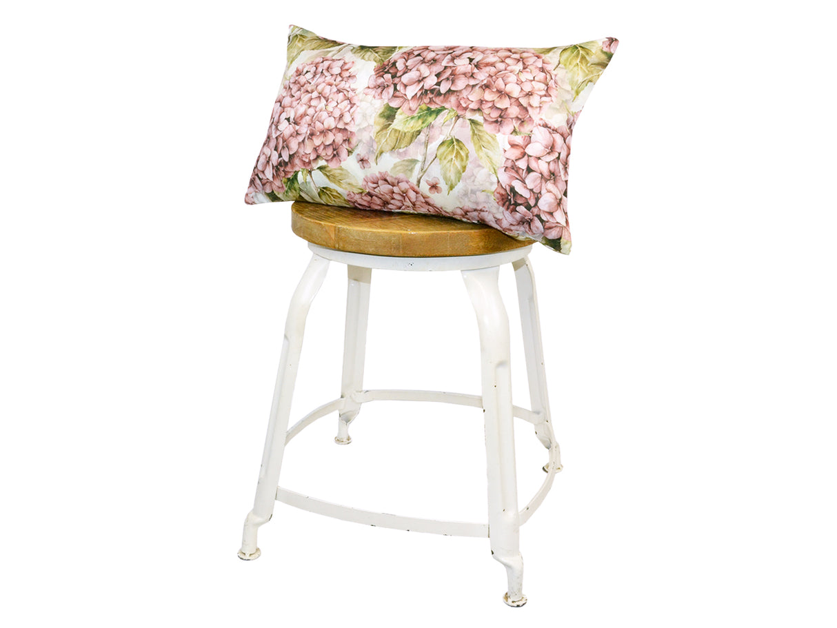 Auf einem Hocker liegt ein rechteckiger Kissenbezug im Landhausstil, bedruckt mit rosa/pinken Hortensien-Blueten.