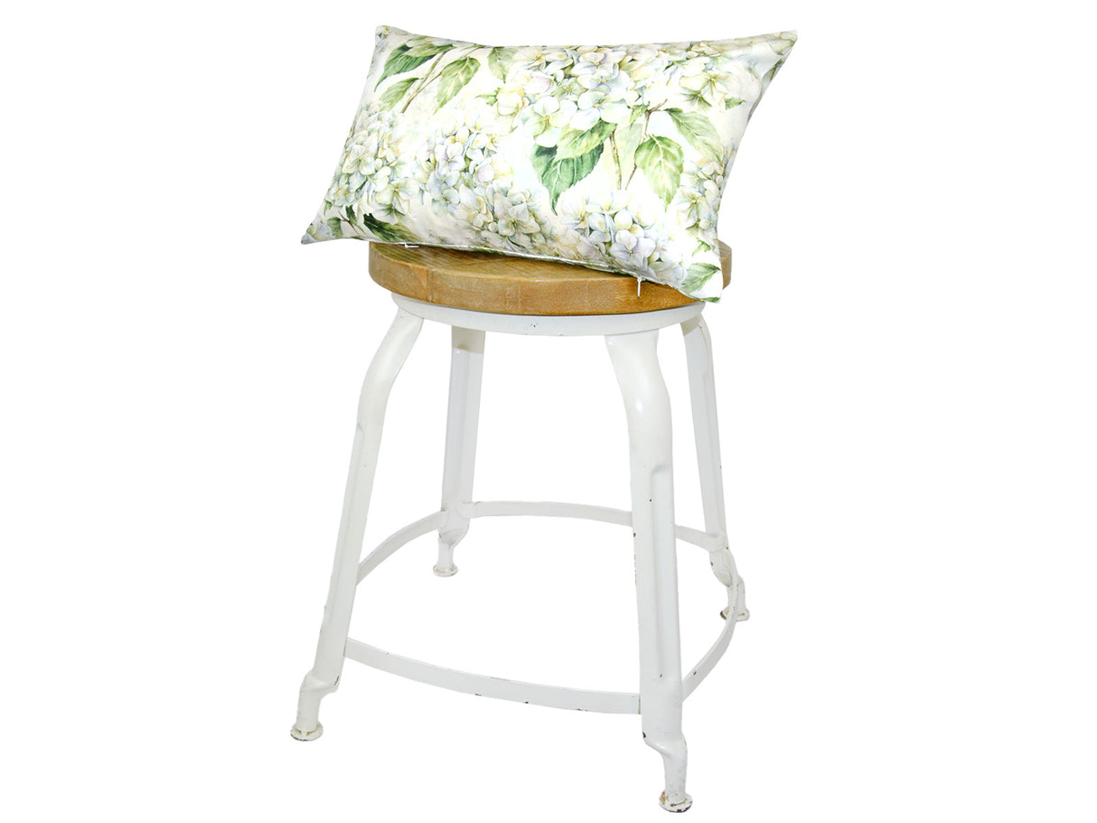 Auf einem Hocker liegt ein rechteckiger Kissenbezug im Landhausstil, bedruckt mit weissen Hortensien-Blueten.