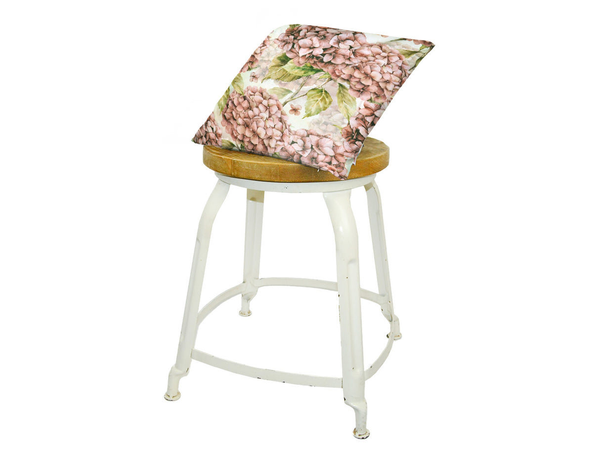 Auf einem Hocker liegt ein quadratischer Kissenbezug im Landhausstil, bedruckt mit rosanen/pinken Hortensien-Blueten.