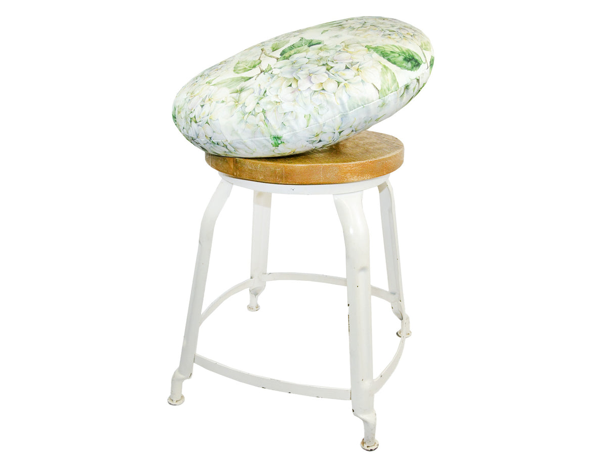Auf einem Hocker liegt ein runder Kissenbezug im Landhausstil, bedruckt mit weissen Hortensien-Blueten.
