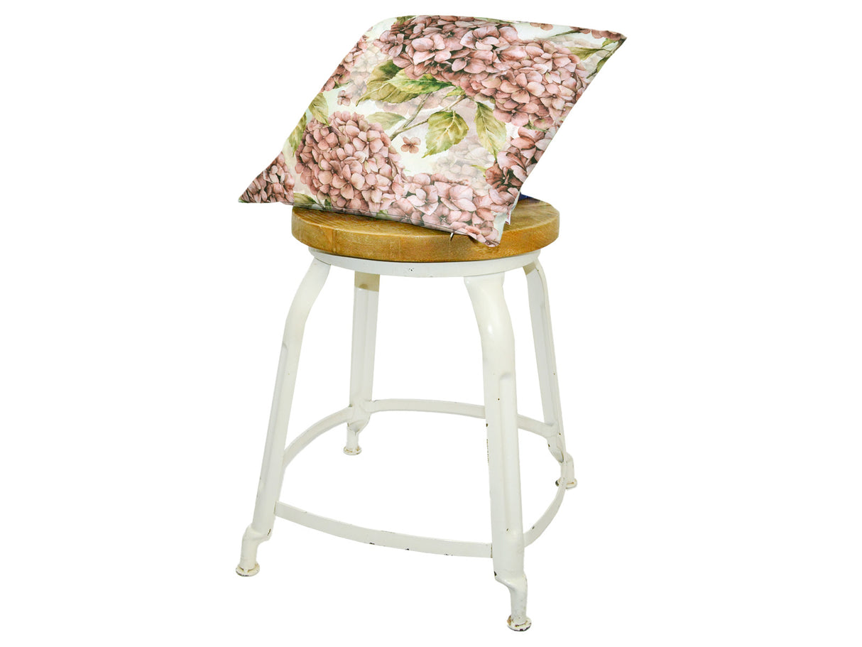 Auf einem Hocker liegt ein quadratischer Kissenbezug im Landhausstil, bedruckt mit rosanen/pinken Hortensien-Blueten.