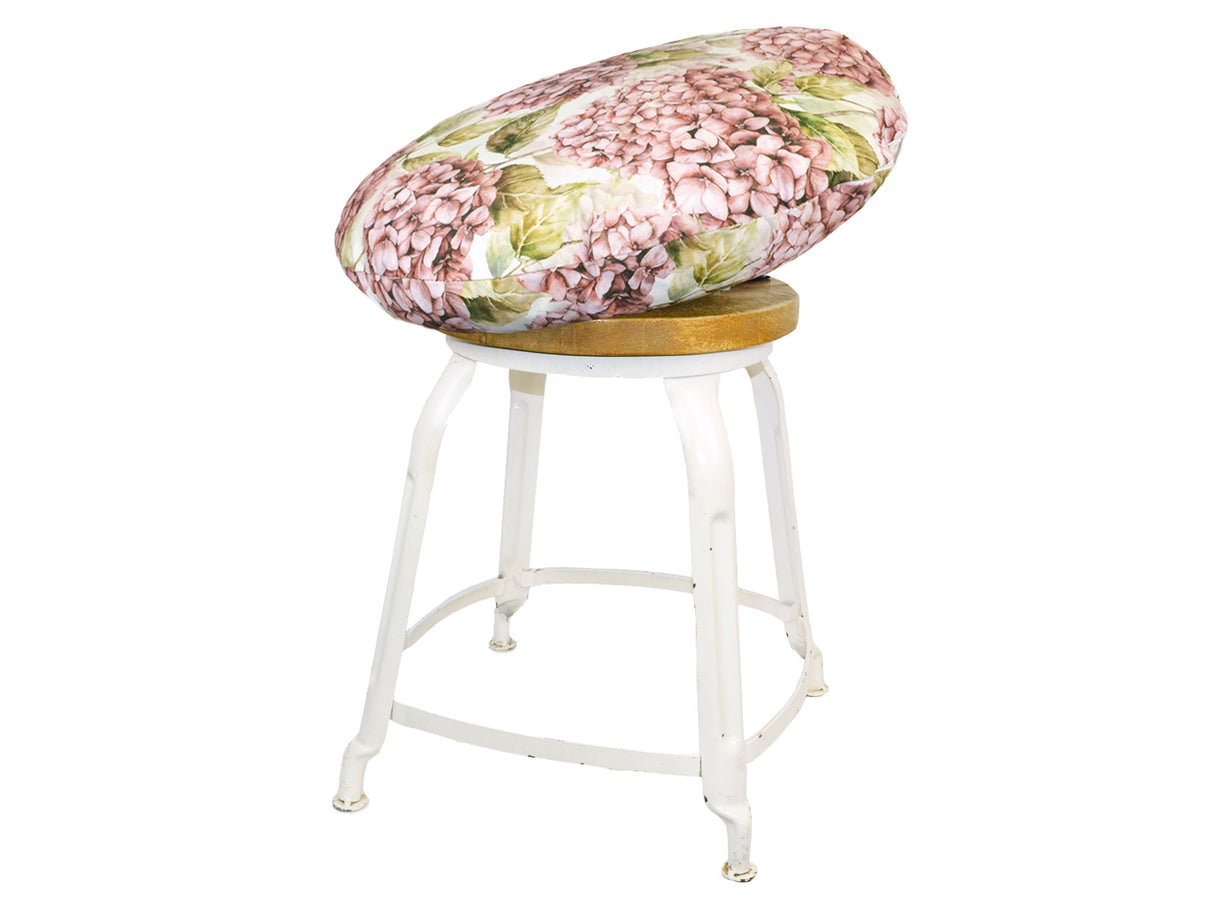 Auf einem Hocker liegt ein runder Kissenbezug im Landhausstil, bedruckt mit rosanen/pinken Hortensien-Blueten.