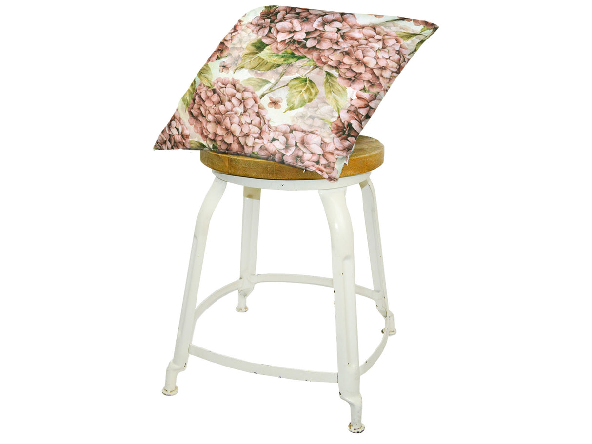 Auf einem Hocker liegt ein quadratischer Kissenbezug im Landhausstil, bedruckt mit rosa/pinken Hortensien-Blueten.