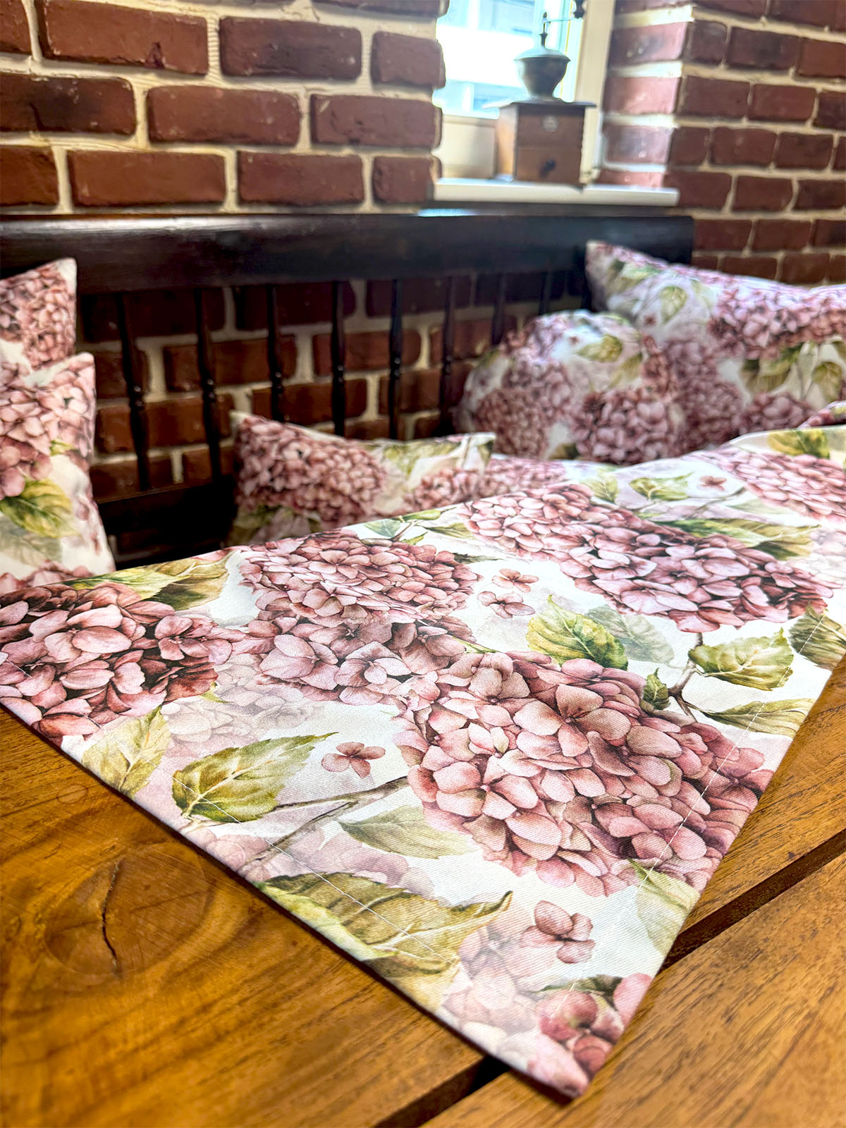 Eine Mitteldecke bedruckt mit rosa/pinken Hortensien auf einem Holztisch.
