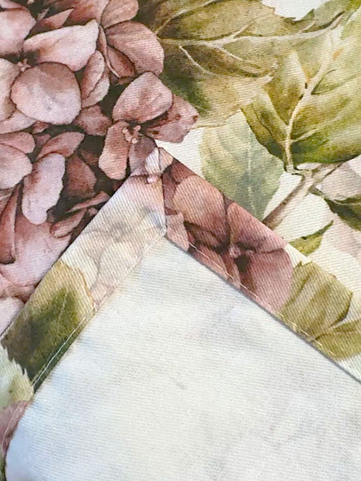 Nahaufnahme einer Briefecke an einer mit rosa/pinken Hortensien bedruckten Tischwaesche.