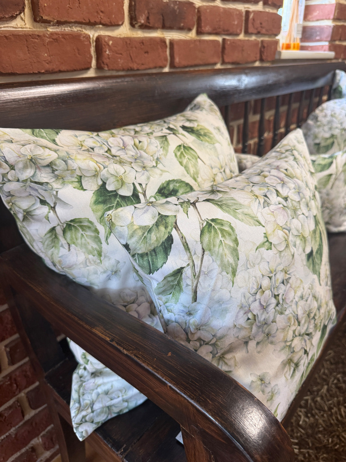 Auf einer dunklen Holzbank sind Kissenbezuege im Landhausstil, bedruckt mit weissen Hortensien-Blueten, drapiert.