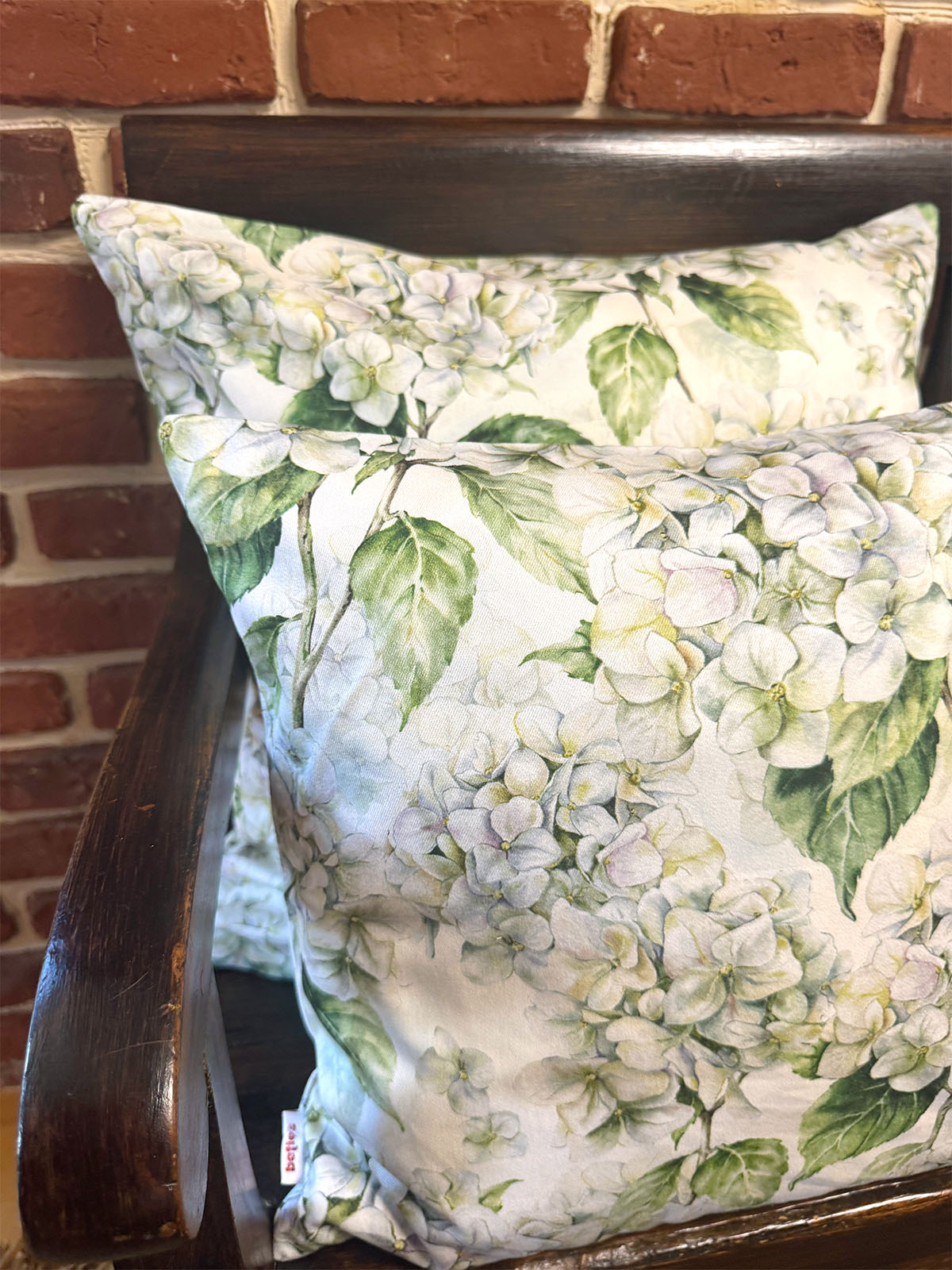 Auf einer dunklen Holzbank sind Kissenbezuege im Landhausstil, bedruckt mit weissen Hortensien-Blueten, drapiert.