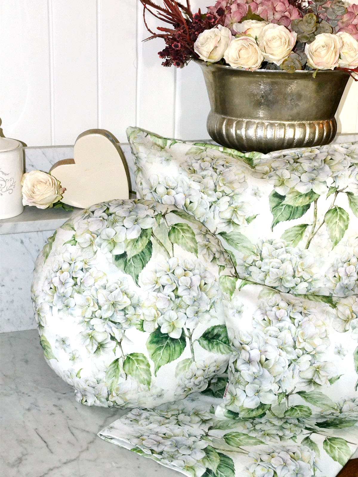 Drei Kissen bezogen mit je einem Kissenbezug im Landhausstil, bedruckt mit weissen Hortensien. Dekoriert auf einer Marmorplatte.