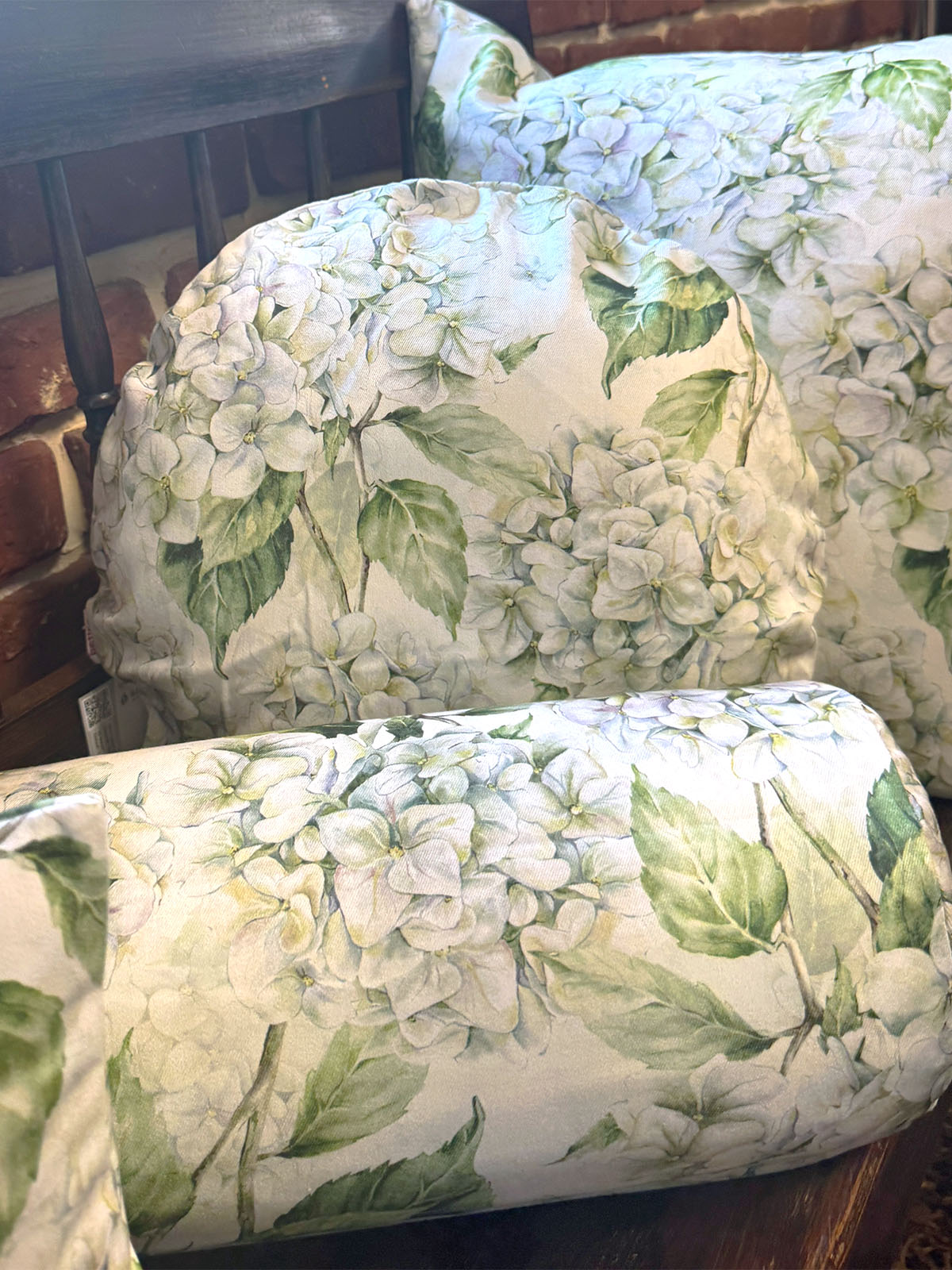 Auf einer dunklen Holzbank sind Kissenbezuege im Landhausstil, bedruckt mit weissen Hortensien-Blueten, drapiert.