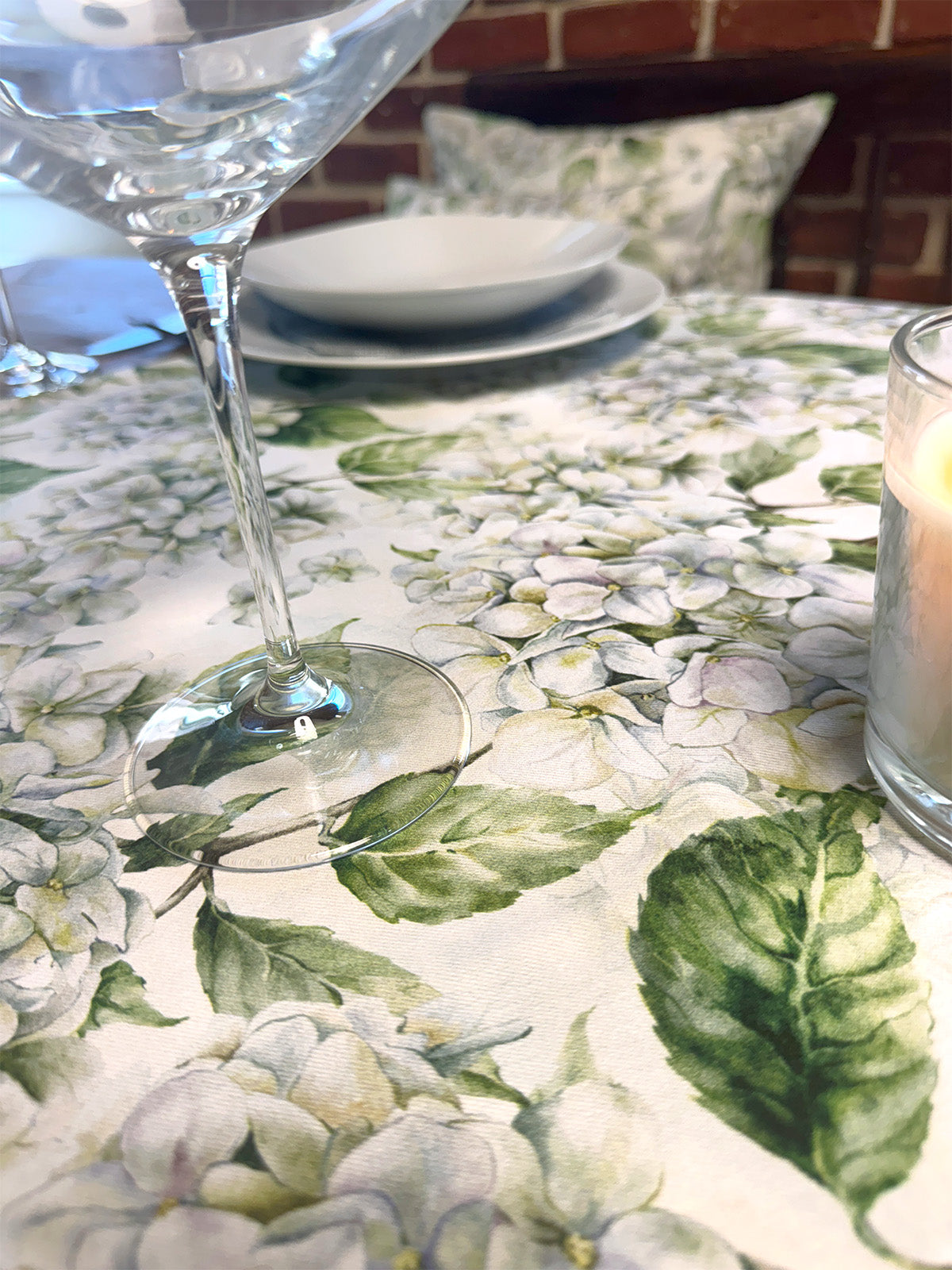 Eine weisse, geblümte Tischdecke bedruckt mit weissen Hortensien auf einem gedeckten Tisch.