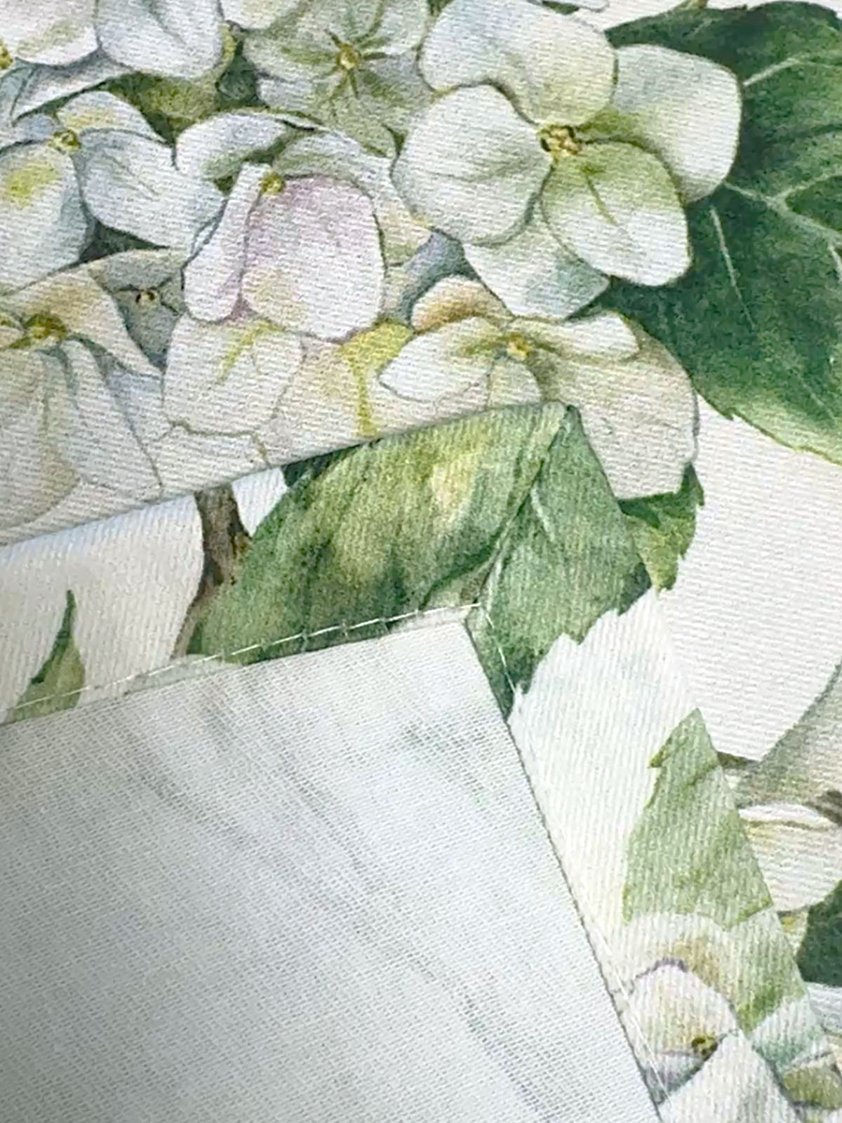 Nahaufnahme einer Briefecke an einer mit weissen Hortensien bedruckten Tischwaesche.