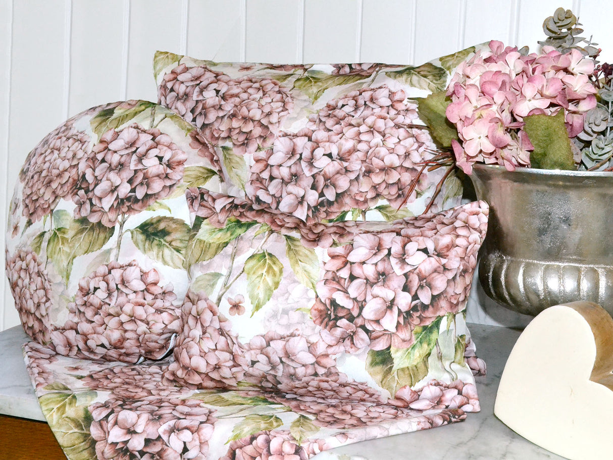 Drei Kissen bezogen mit je einem Kissenbezug im Landhausstil, bedruckt mit rosa/pinken Hortensien. Dekoriert auf einer Marmorplatte.
