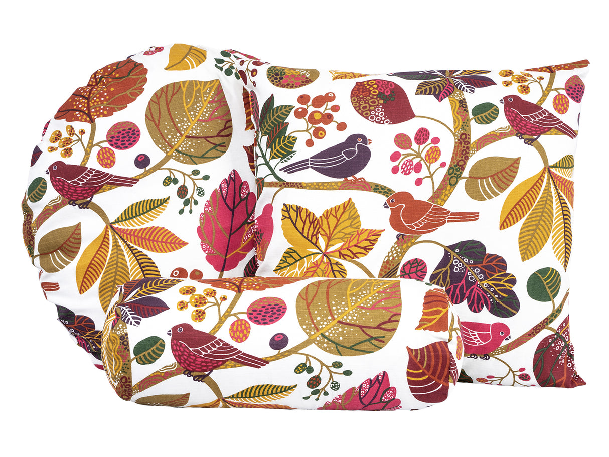 Ein runder und ein quadratischer Kissenbezug und ein Nackenrollenbezug mit bunten Blaettern und Zweigen auf weissem Hintergrund.