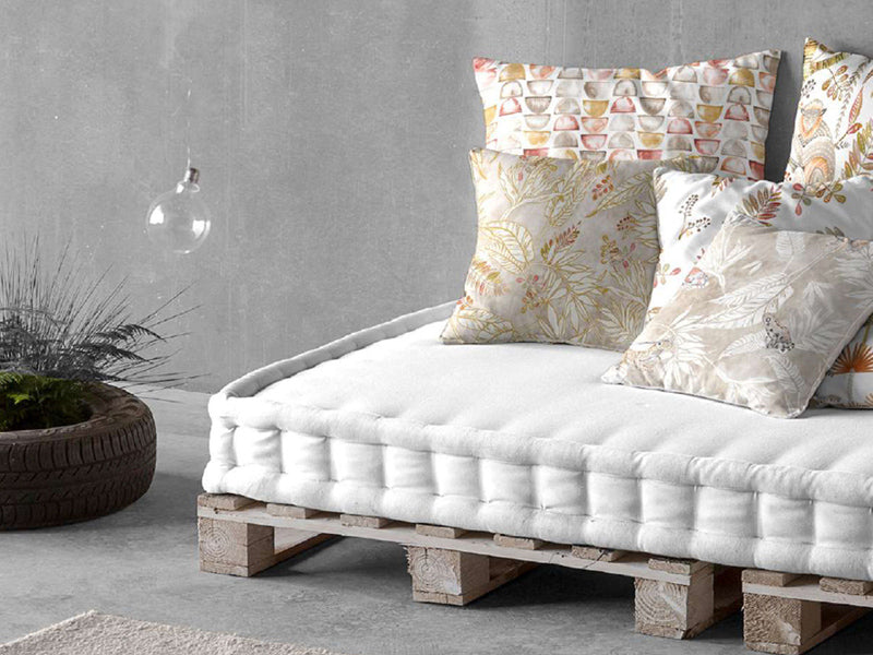 Palettensofa mit darauf drapierten quadratischen Kissen. Dies sind mit verschiedenen Kissenhuellen in Erdfarben bezogen.