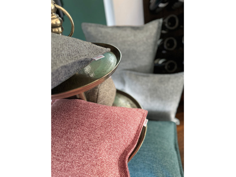 Fuenf Kissen im Raum drapiert, bezogen mit Boucle Kissenbezuegen in den Farben Grau, Rot und Petrol.