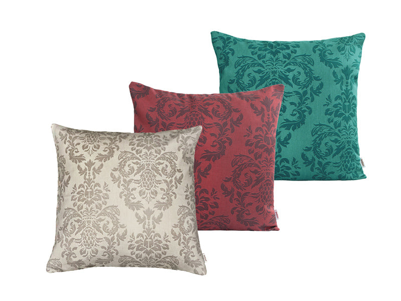 Drei quadratische Kissen hintereinander, bezogen mit Kissenbezuegen in den Farben Beige, Rot und Petrol. Bedruckt sind die Bezuege mit barocken Ornamenten in der jeweiligen Farbe, nur etwas dunkler.