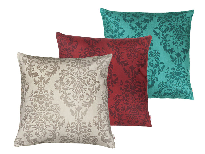 Drei quadratische Kissen hintereinander, bezogen mit Kissenbezuegen in den Farben Beige, Rot und Petrol. Bedruckt sind die Bezuege mit barocken Ornamenten in der jeweiligen Farbe, nur etwas dunkler.
