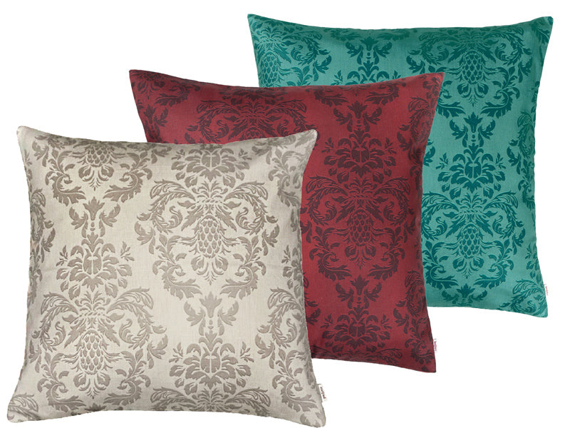 Drei quadratische Kissen hintereinander, bezogen mit Kissenbezuegen in den Farben Beige, Rot und Petrol. Bedruckt sind die Bezuege mit barocken Ornamenten in der jeweiligen Farbe, nur etwas dunkler.
