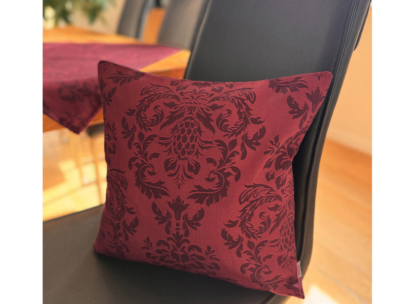 Auf einem schwarzen Lederstuhl, lehnt ein Kissen, bezogen mit einem roten Kissenbezug, der mit barocken Ornamenten in einem dunkleren Roten, bedruckt ist.
