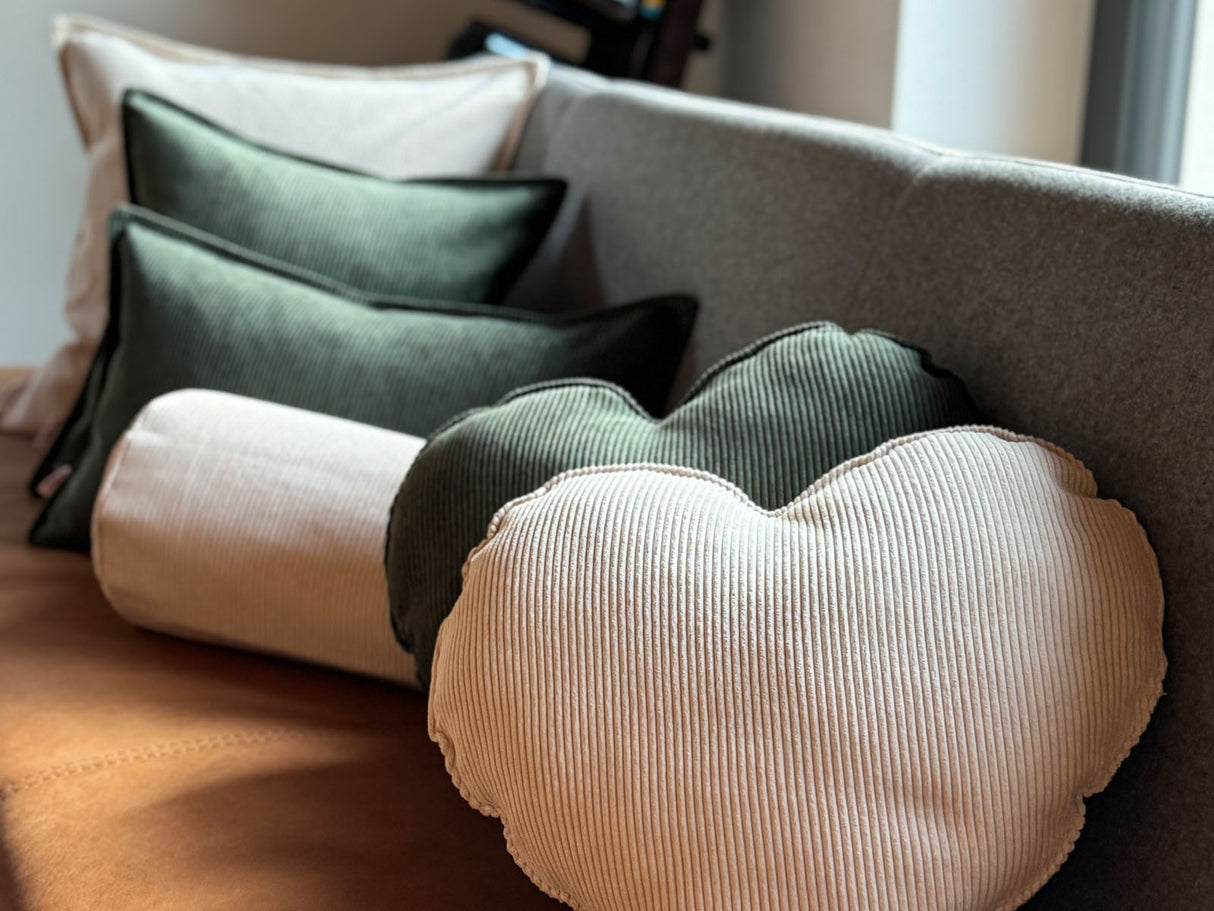 Auf einer Esszimmerbank liegen zwei Herz-Kissen aus Cord-Samt in den Farben bamboo-gruen und kreide-beige.