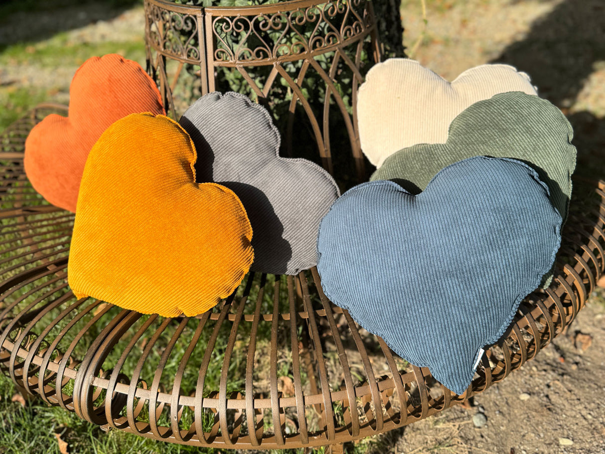 Auf einer Metallbank im Garten liegen sechs gefuellte Herzkissen ca. 35x40 cm aus Cord-Samt, Deko Formkissen in den uni-Farben blau, beige, gelb, orange, gruen und grau - aus der beties "HYggelig No.1" Kollektion.