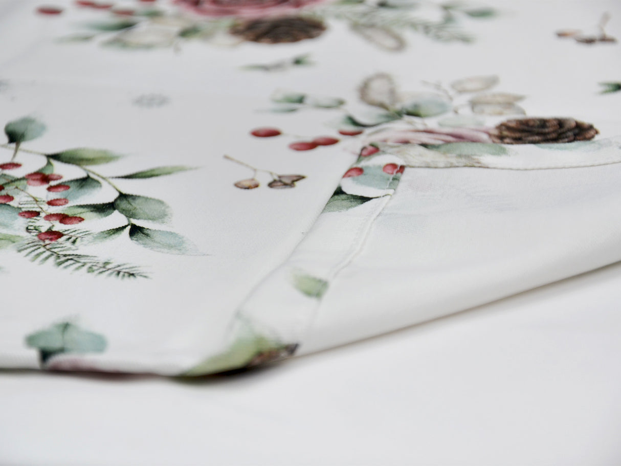Detailansicht der Kuvertecke einer weissen Tischdecke – Winterdeko mit gefrosteten Rosen in mauve, Kieferzapfen, Beeren und Zweigen – 100% Baumwolle – aus der beties Magie des Winters "Frost-Rose" Kollektion.