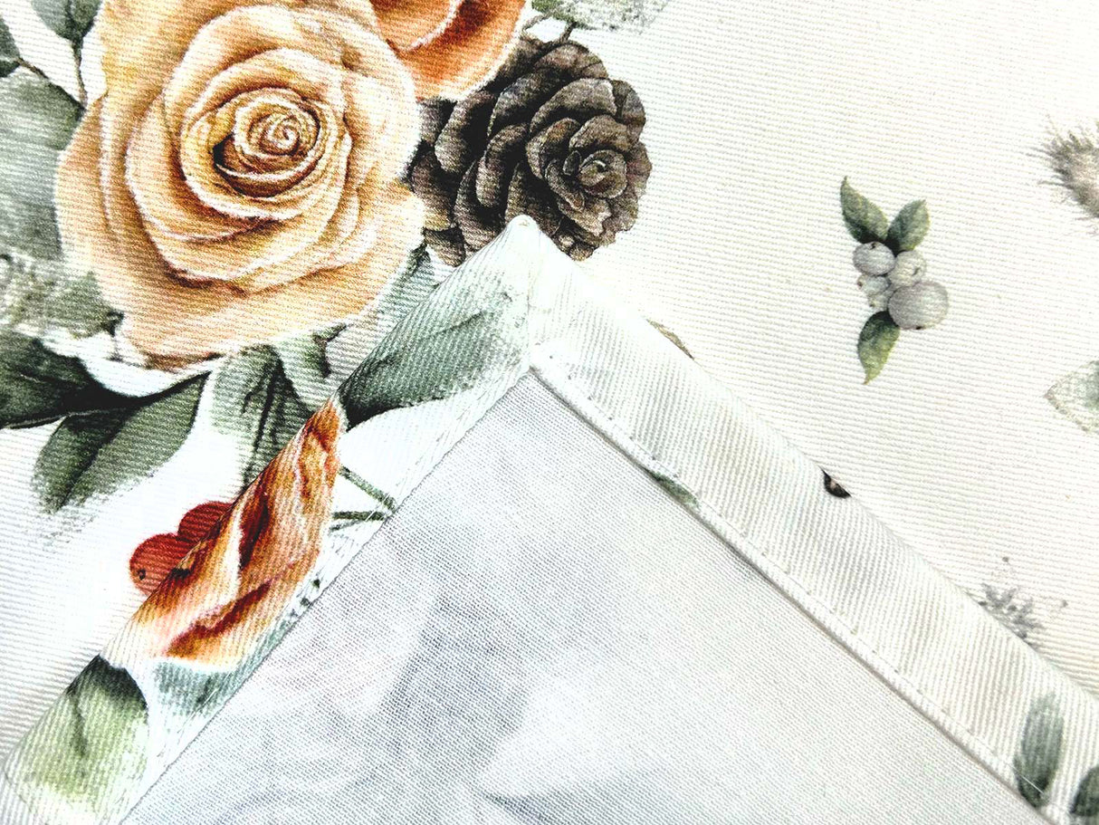 Detailansicht der Kuvertecke einer weissen Tischdecke – Winterdeko mit gefrosteten Rosen in orange, Kieferzapfen, Beeren und Zweigen – 100% Baumwolle – aus der beties Magie des Winters "Frost-Rose" Kollektion.