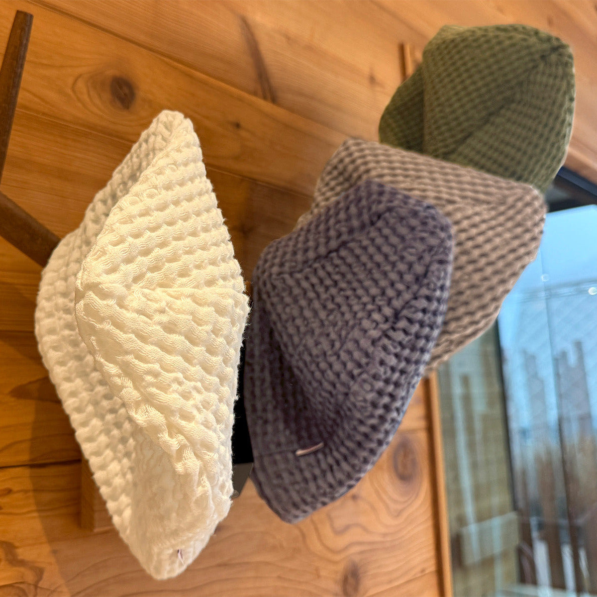 In einer Sauna haengen an einer Holzwand an einem Hirschgeweih vier Waffelpique-Sauna-Beanie aus Baumwoll- Leinenmix in den Farben Gletscher-weiss, Fjord-blau, Nebel-grau und Salbei-gruen.