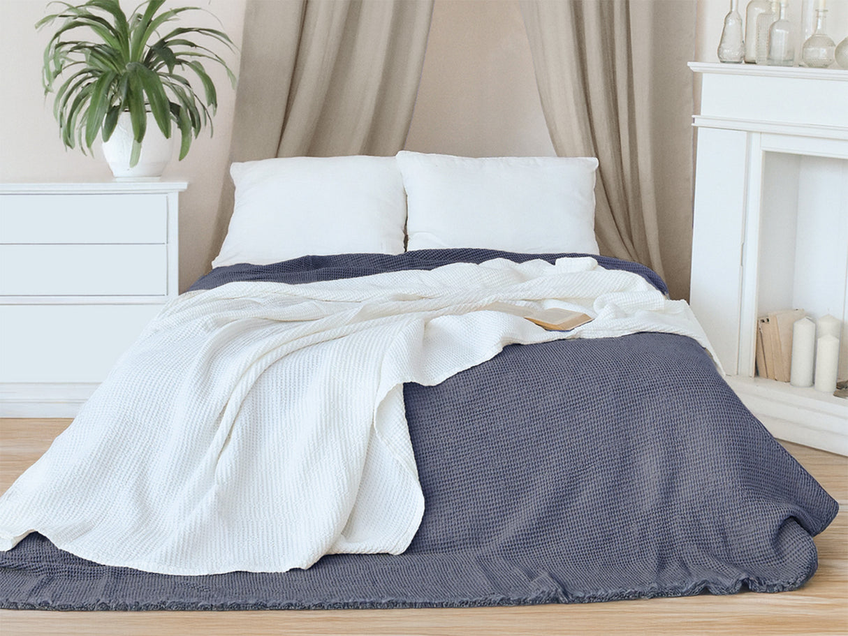 In einem Schlafzimmer liegt eine Gletscher-weisse und eine Fjord-blaue Tagesdecke aus der beties "PUR.NATURE" Serie auf einem Bett ausgebreitet.