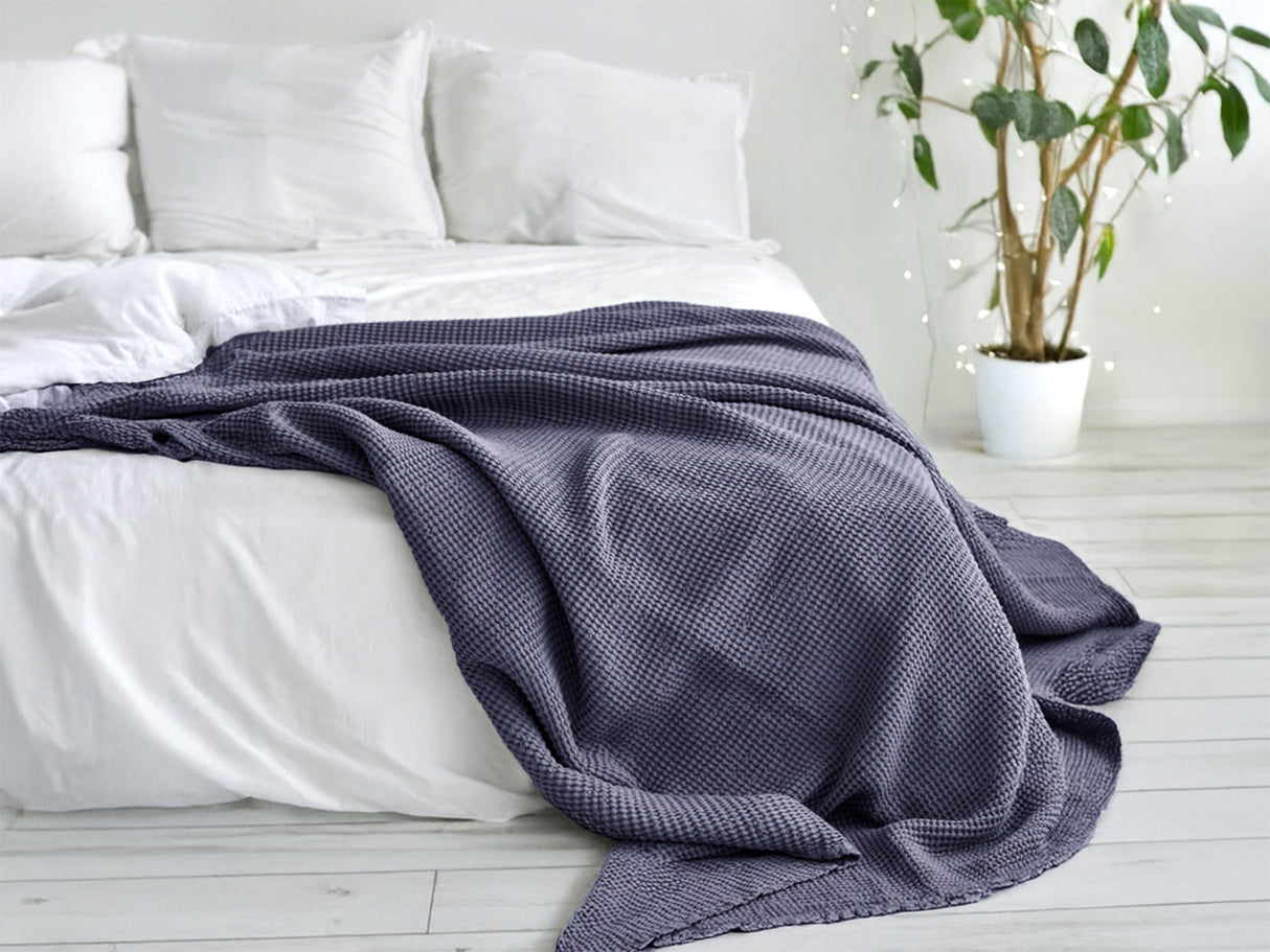 In einem Schlafzimmer liegt eine Fjord-blaue Tagesdecke aus der beties "PUR.NATURE" Serie auf einem Bett ausgebreitet.