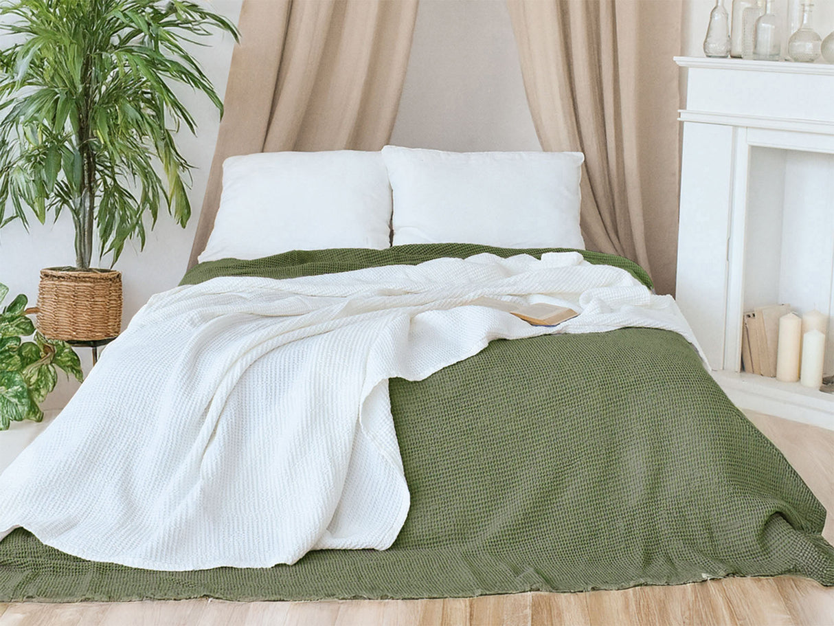 In einem Schlafzimmer liegt eine Gletscher-weisse und eine Salbei-gruene Tagesdecke aus der beties "PUR.NATURE" Serie auf einem Bett ausgebreitet.