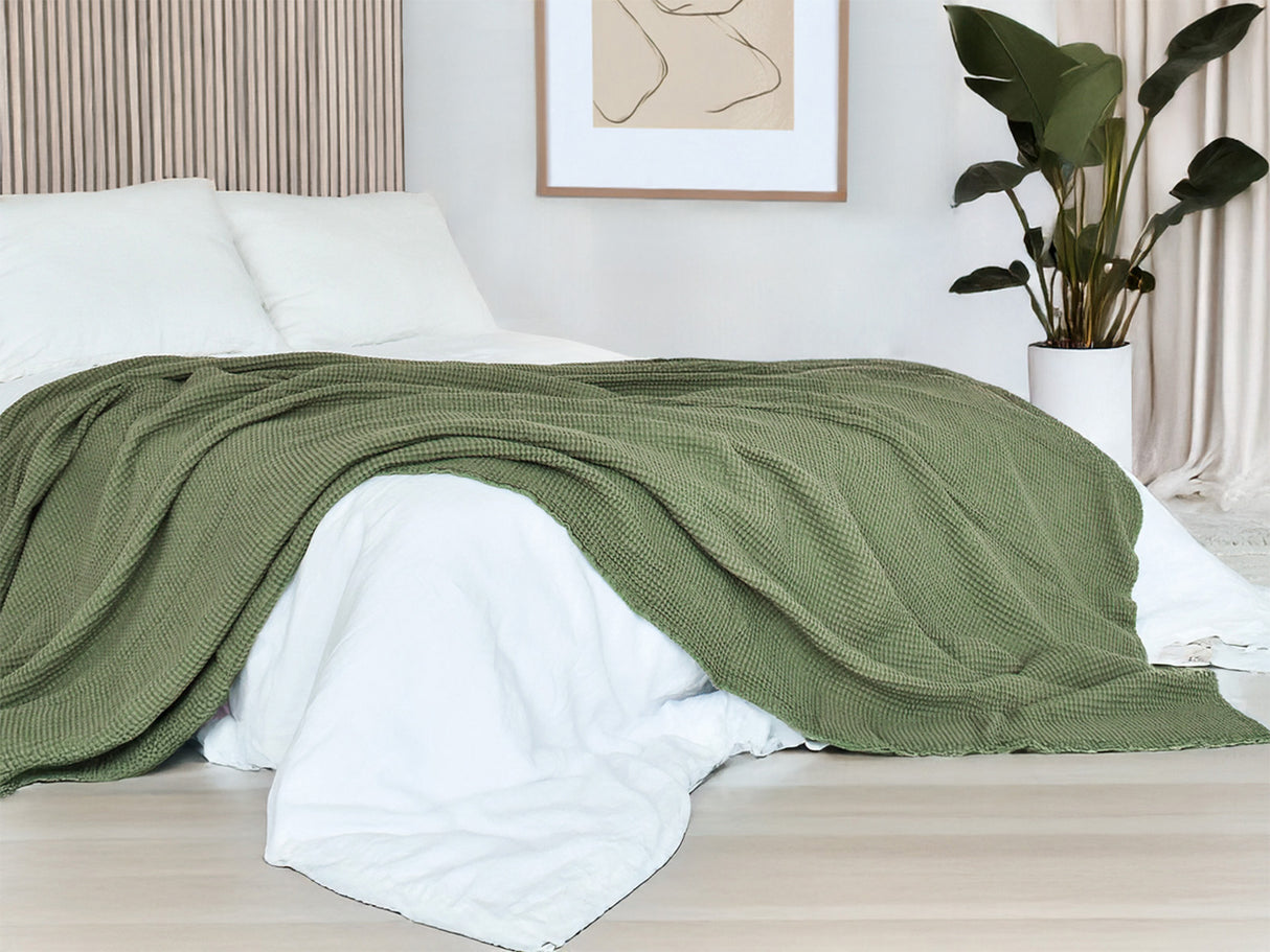 In einem Schlafzimmer liegt eine Salbei-gruene Tagesdecke aus der beties "PUR.NATURE" Serie auf einem Bett ausgebreitet.